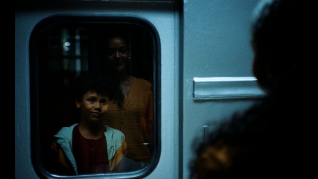 Reflexo em uma janela de trem escurecida mostrando uma mãe sorrindo atrás de seu filho menino. Cena do filme Despedidas da campanha de Dia das Mães do Boticário.