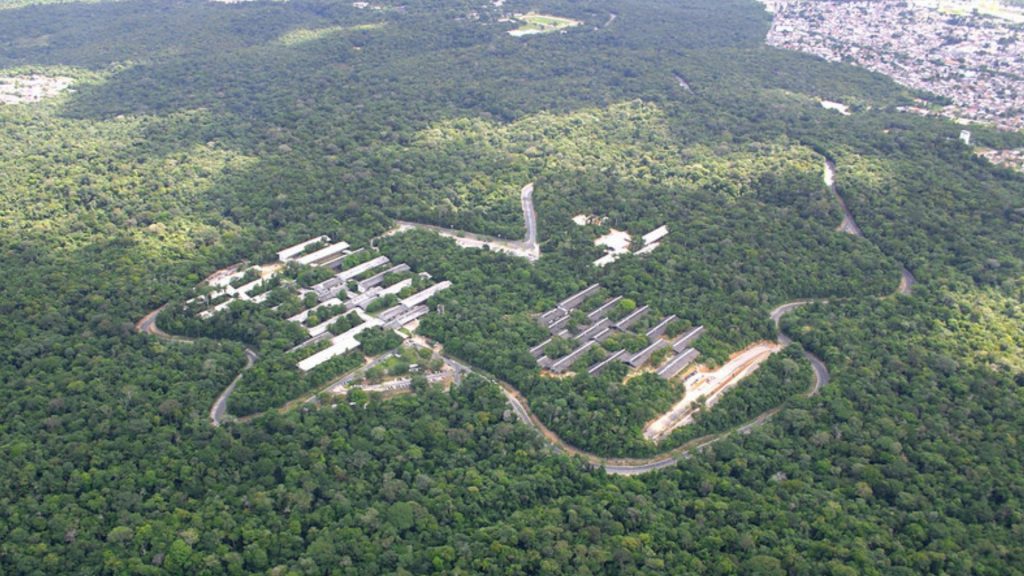 Vista aérea do campus da Universidade Federal do Amazonas (UFAM) em Manaus, com prédios e pavilhões acadêmicos integrados à densa floresta amazônica urbana, cortados por vias de acesso sinuosas