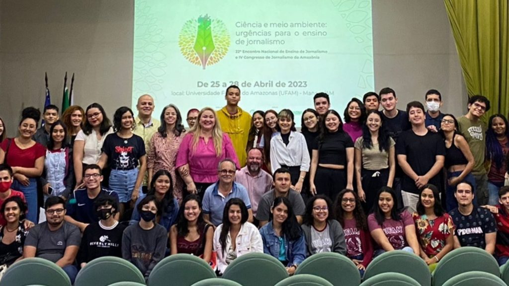 Grande grupo de estudantes e professores sorridentes posando para uma foto coletiva em um auditório. Ao fundo, o telão indica o "22º Encontro Nacional de Ensino de Jornalismo e IV Congresso de Jornalismo da Amazônia".