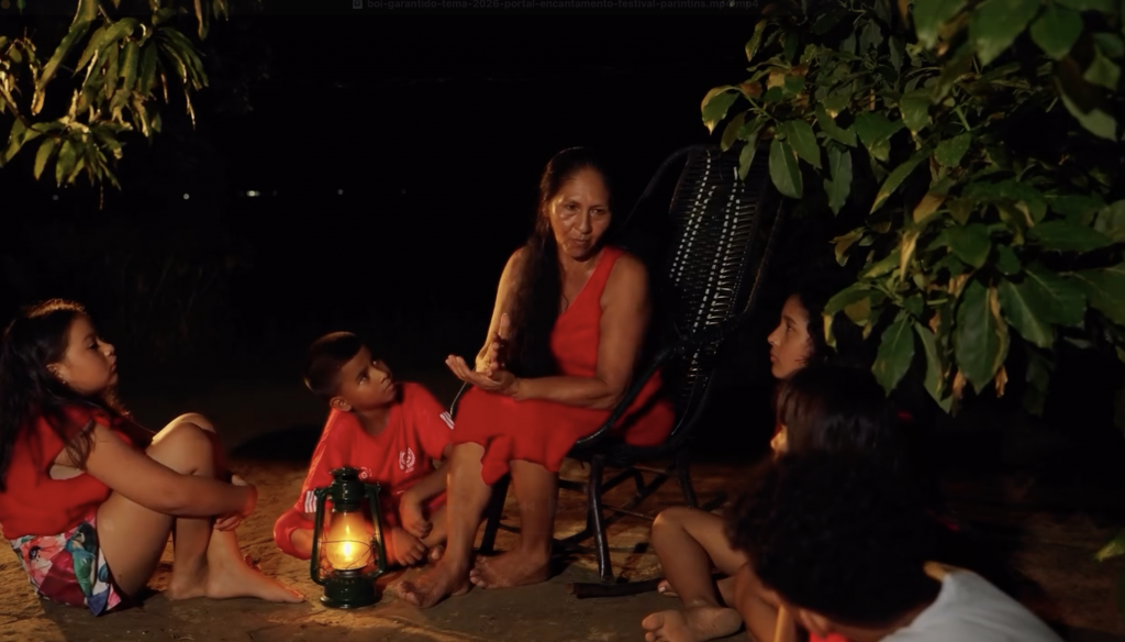 Ansiã, idosa da floresta amazônica, conta histórias dos encantados para crianças ao redor de fogueira iluminada durante a noite, cercada por vegetação.